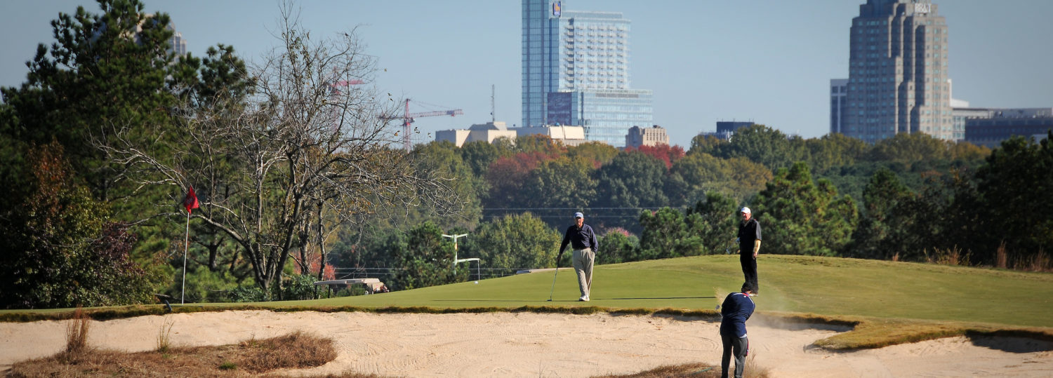 Golfers in a sand trap, with the Raleigh skyline in the background.