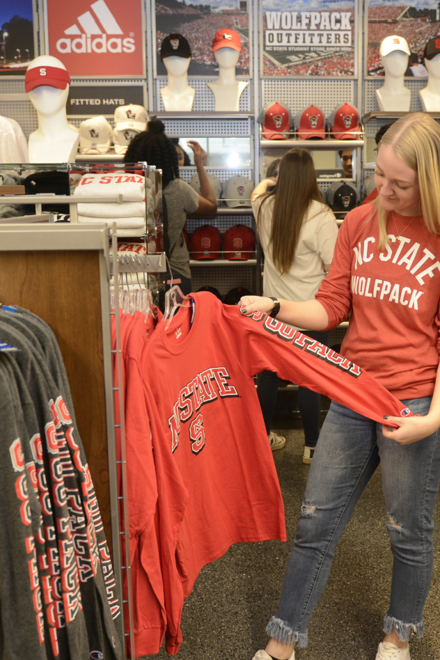 A student examines an NC State sweatshirt at Wolfpack Outfitters.